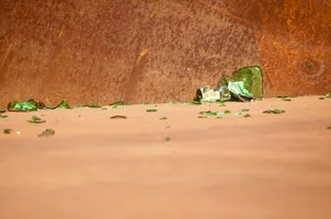 A green glass container broken into so many pieces that its original shape is difficult to guess.