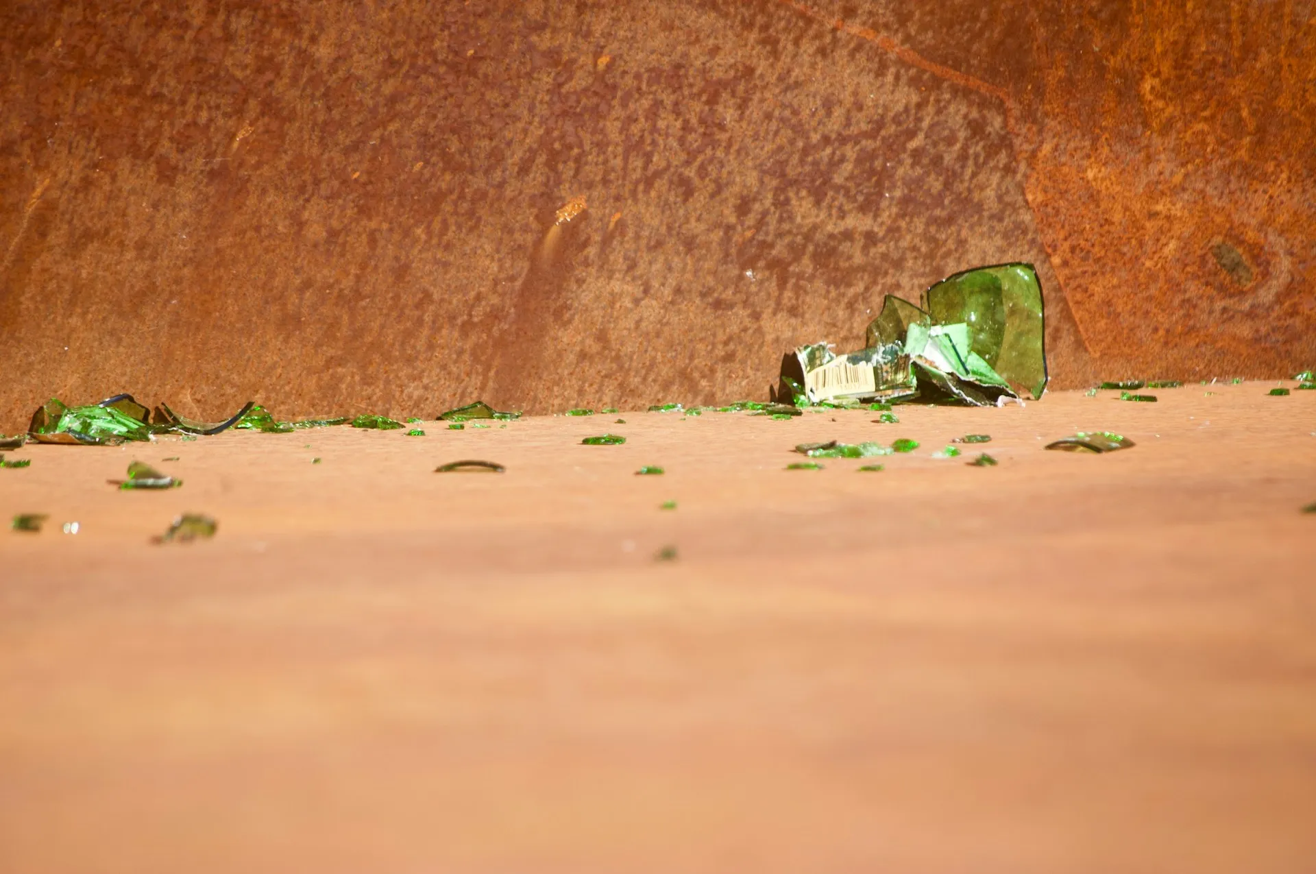 A green glass container broken into so many pieces that its original shape is difficult to guess.