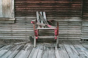 A wooden chair missing the left half of its back and most of that arm. A couple of planks possibly meant for the back are leaning over the seat.