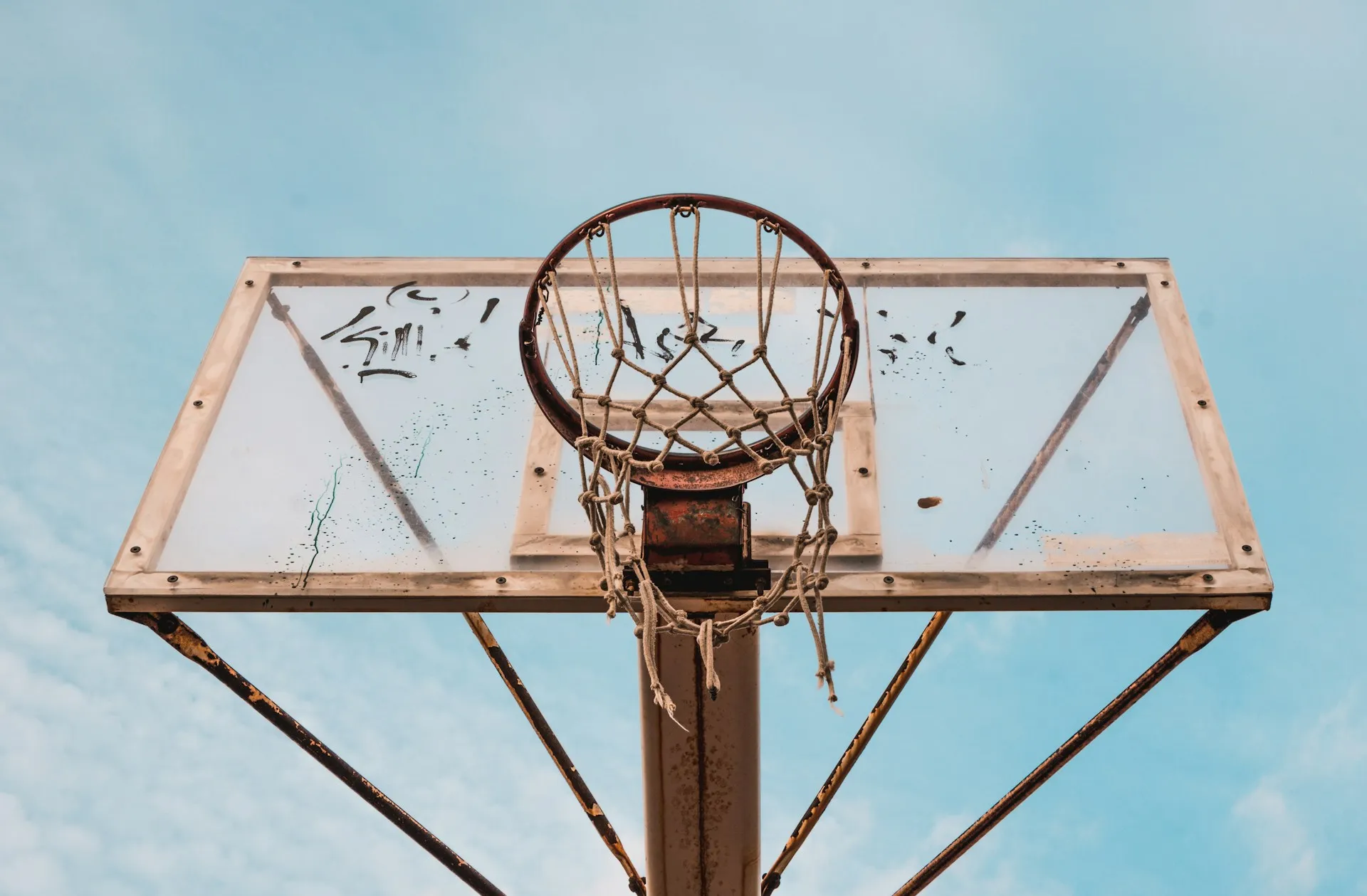 A rusted, washed-out basketball hoop with a partially-detached net.