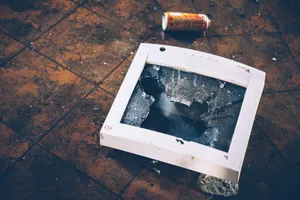 A CRT monitor on a floor facing upward, its glass thoroughly shattered.