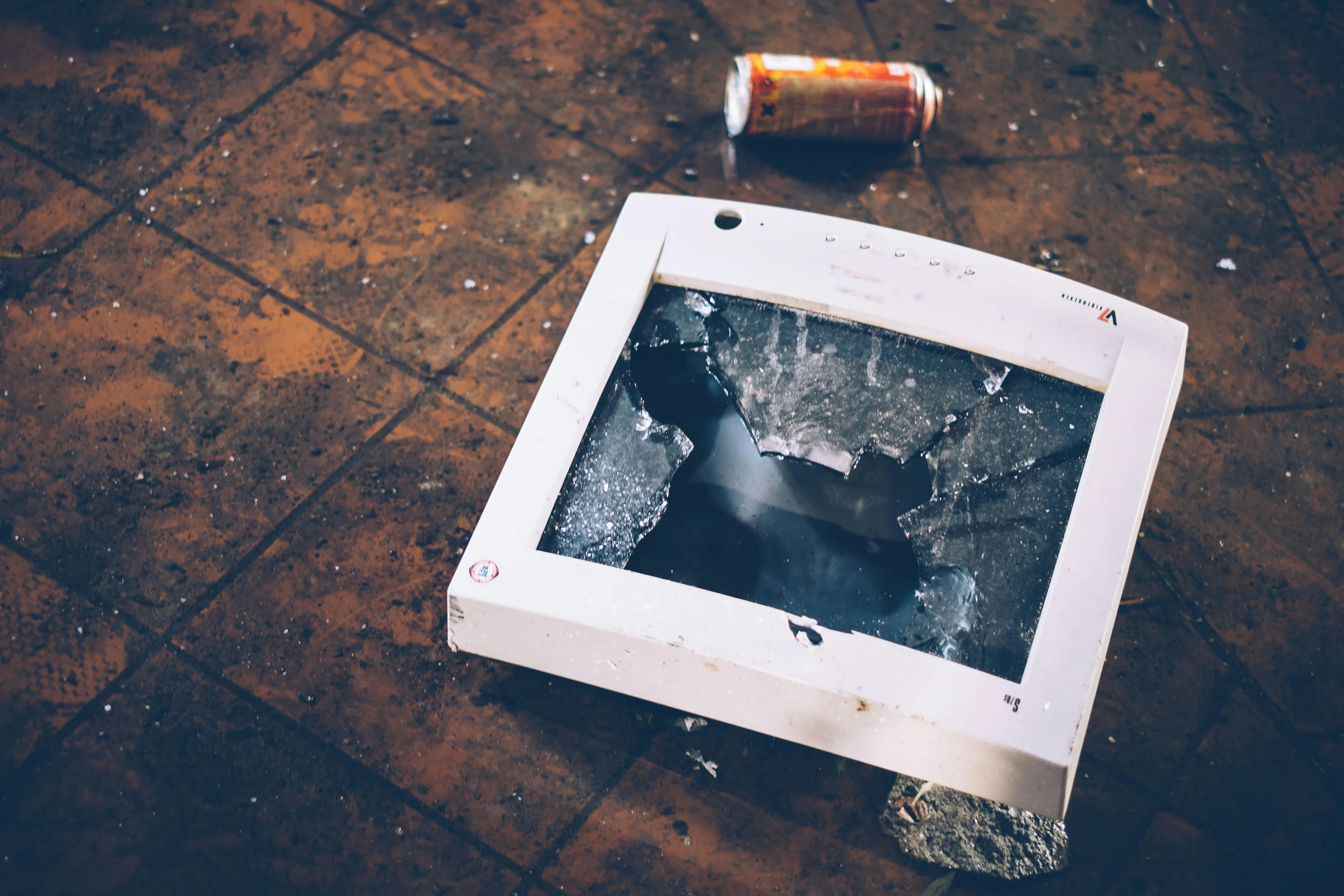 A CRT monitor on a floor facing upward, its glass thoroughly shattered.