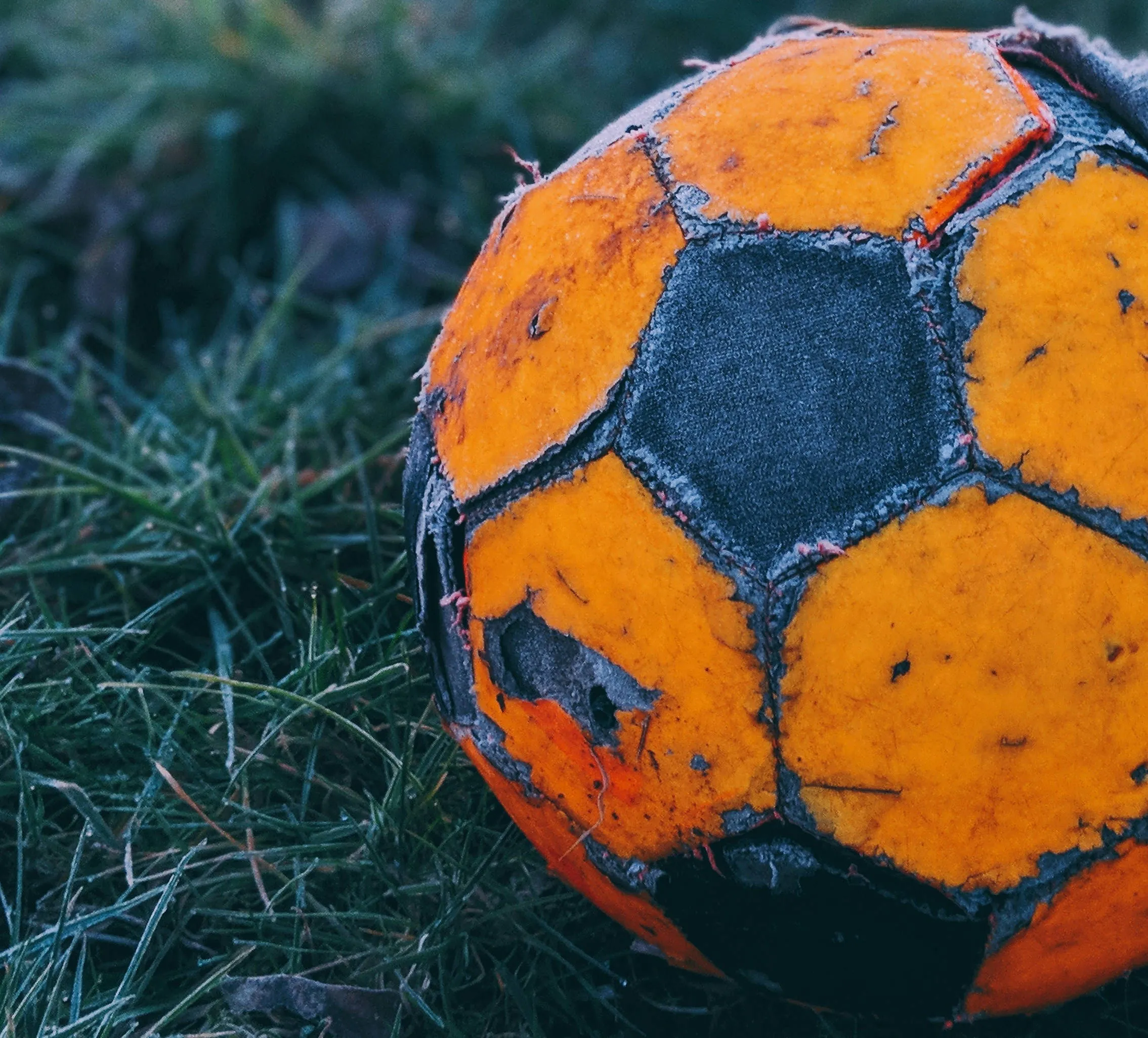 An orange and black soccer ball, with some of its pieces torn or separating.