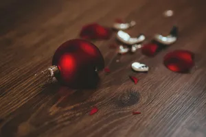 A shiny red ball ornament, part of which has shattered into many pieces across a wood surface.