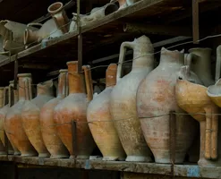 A shelf filled with clay vases, some of which have been broken at the neck or halfway up the body.